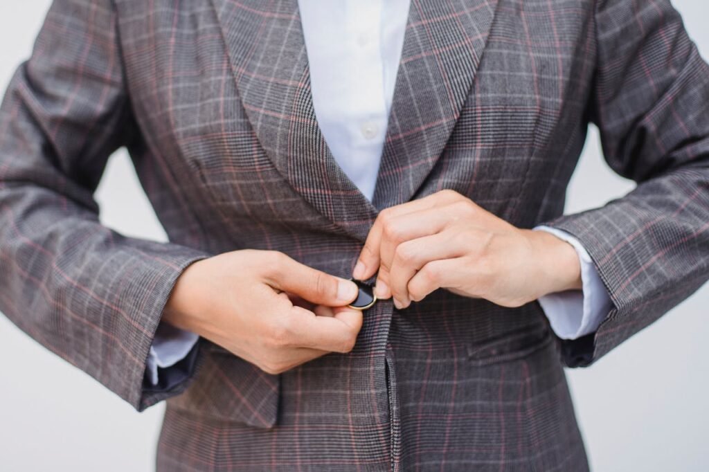 Close-up of a person buttoning a plaid blazer, showcasing professional attire.