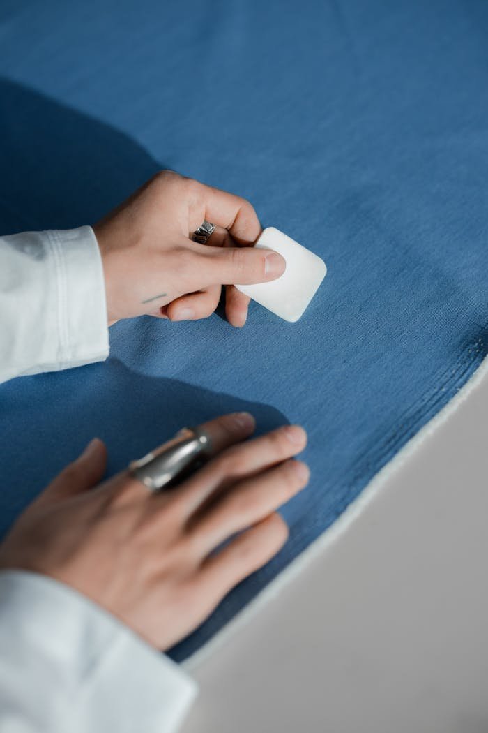 Close-up of a tailor marking blue fabric with chalk, showcasing craftsmanship.